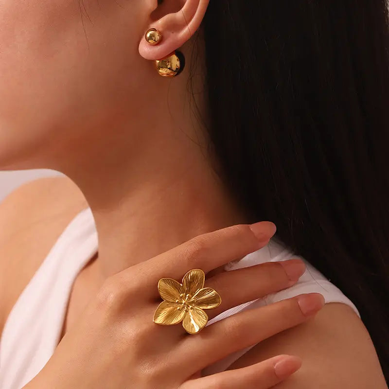 Model wearing a gold hibiscus flower ring with detailed petals on her finger, paired with simple gold earrings, showcasing an elegant and polished look.