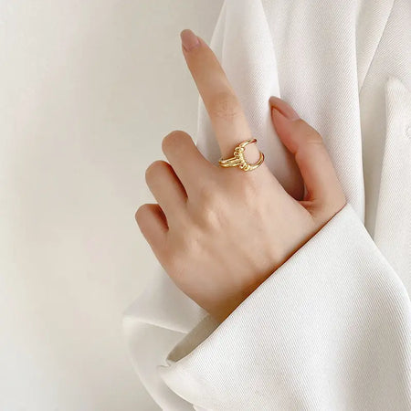 Woman wearing the Knot Gold Ring, featuring a unique open-ended design with a central knot detail, crafted in polished gold-tone metal. This high trending accessory adds a touch of modern elegance and sophistication, perfect for any occasion. She is dressed in a white outfit, highlighting the ring's stylish appeal.