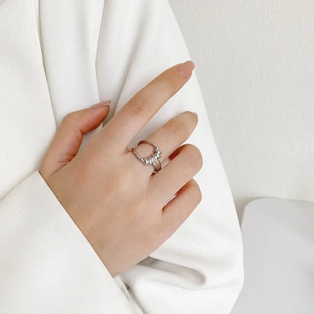Woman wearing the Twist Silver Adjustable Ring, featuring a unique open-ended design with a central knot detail, crafted in polished silver-tone metal. This high trending accessory adds a touch of modern elegance and sophistication, perfect for any occasion. She is dressed in a white outfit, highlighting the ring's stylish appeal.