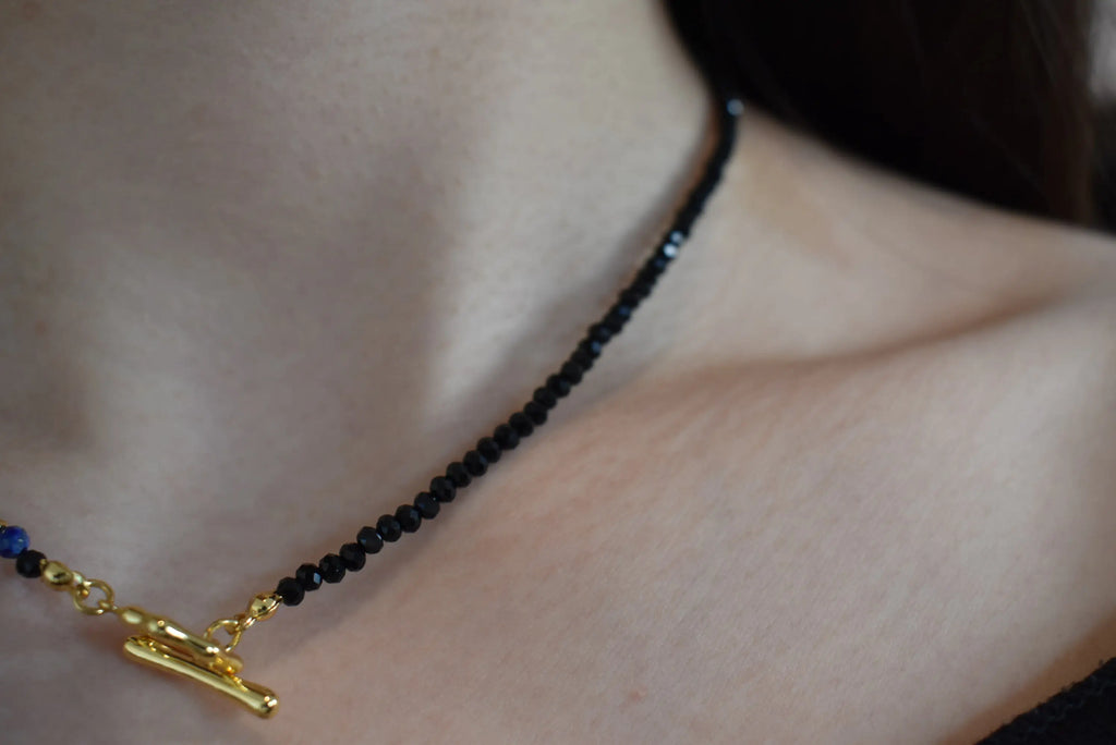 Close-up view of the Lapis Lazuli Black Spinel Crystal Necklace with a focus on the black spinel beads and gold toggle clasp, displayed on a model’s neck.