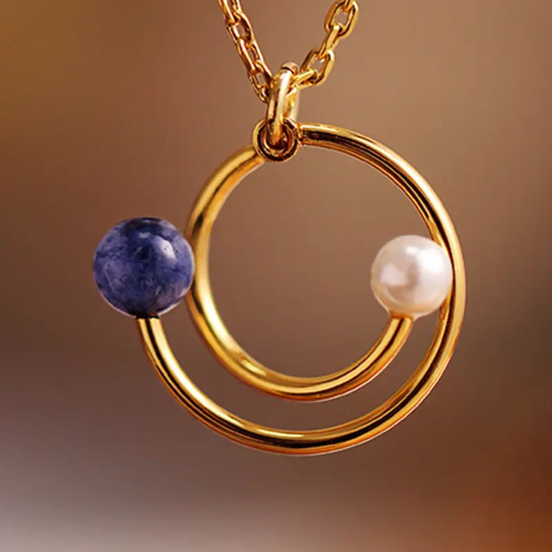 Close-up of the Anais & Aimee Lapis Lazuli Drop Necklace, featuring a gold chain with interlocking circular pendants adorned with a deep blue lapis lazuli stone and a lustrous white pearl. Ideal for adding a touch of elegance and sophistication to any outfit.