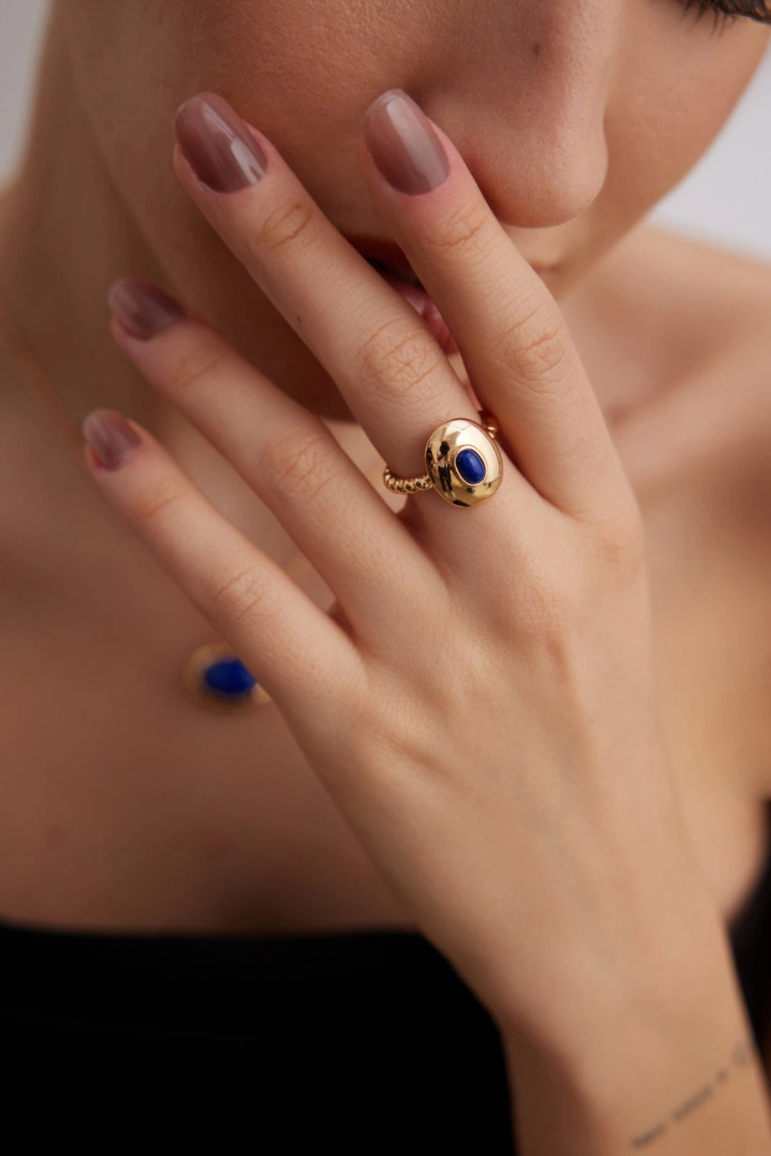 Close-up of a hand wearing a gold ring with a blue gemstone, blurred background