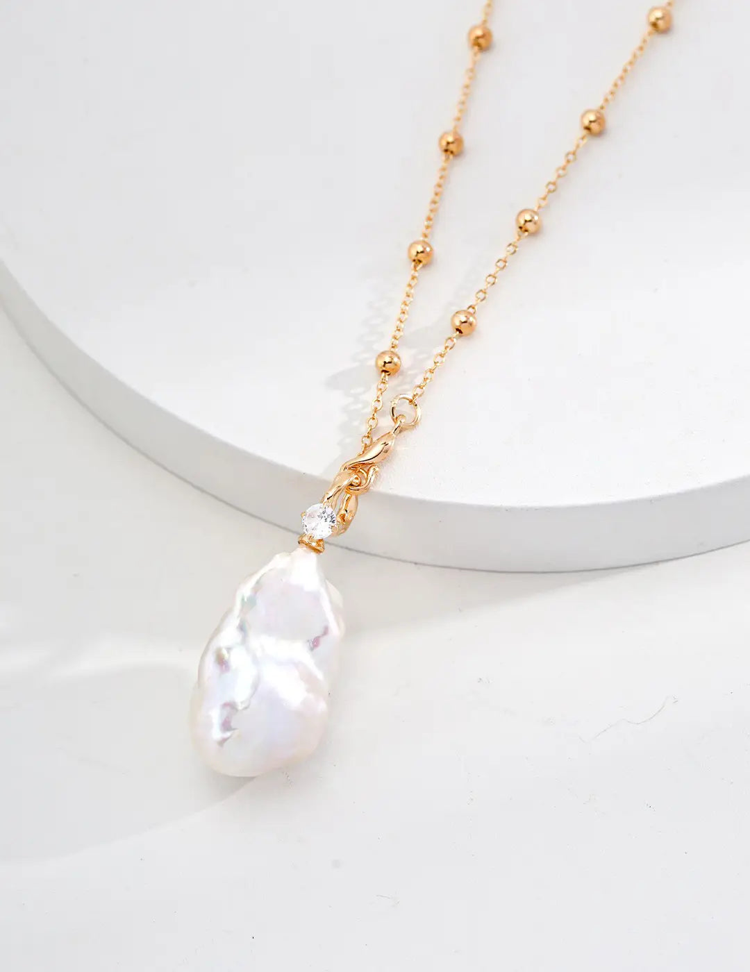 Close-up view of the Luxury Baroque Pearl Necklace displayed elegantly on a minimalist white surface, showcasing its lustrous pearl pendant and delicate gold chain.