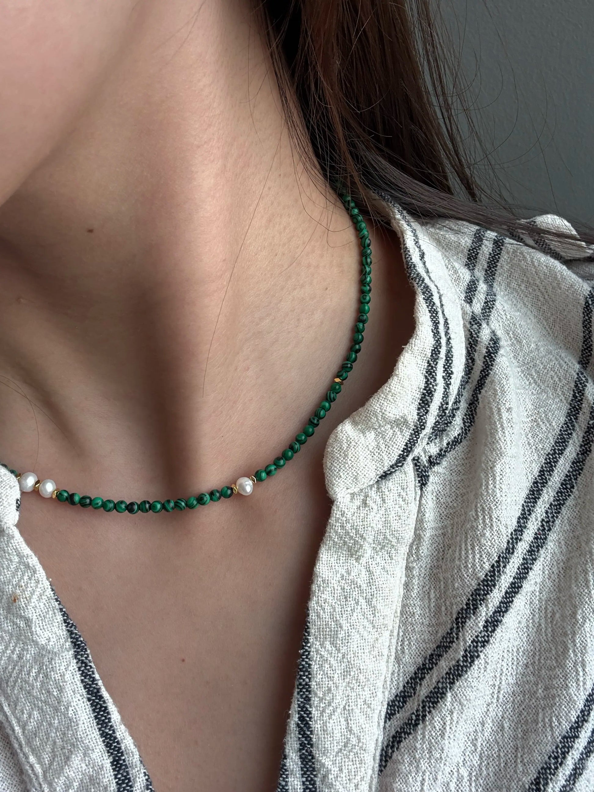 Close-up of woman wearing malachite and pearl necklace with linen shirt in London.