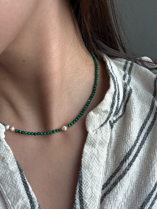 Close-up of woman wearing malachite and pearl necklace with linen shirt in London.