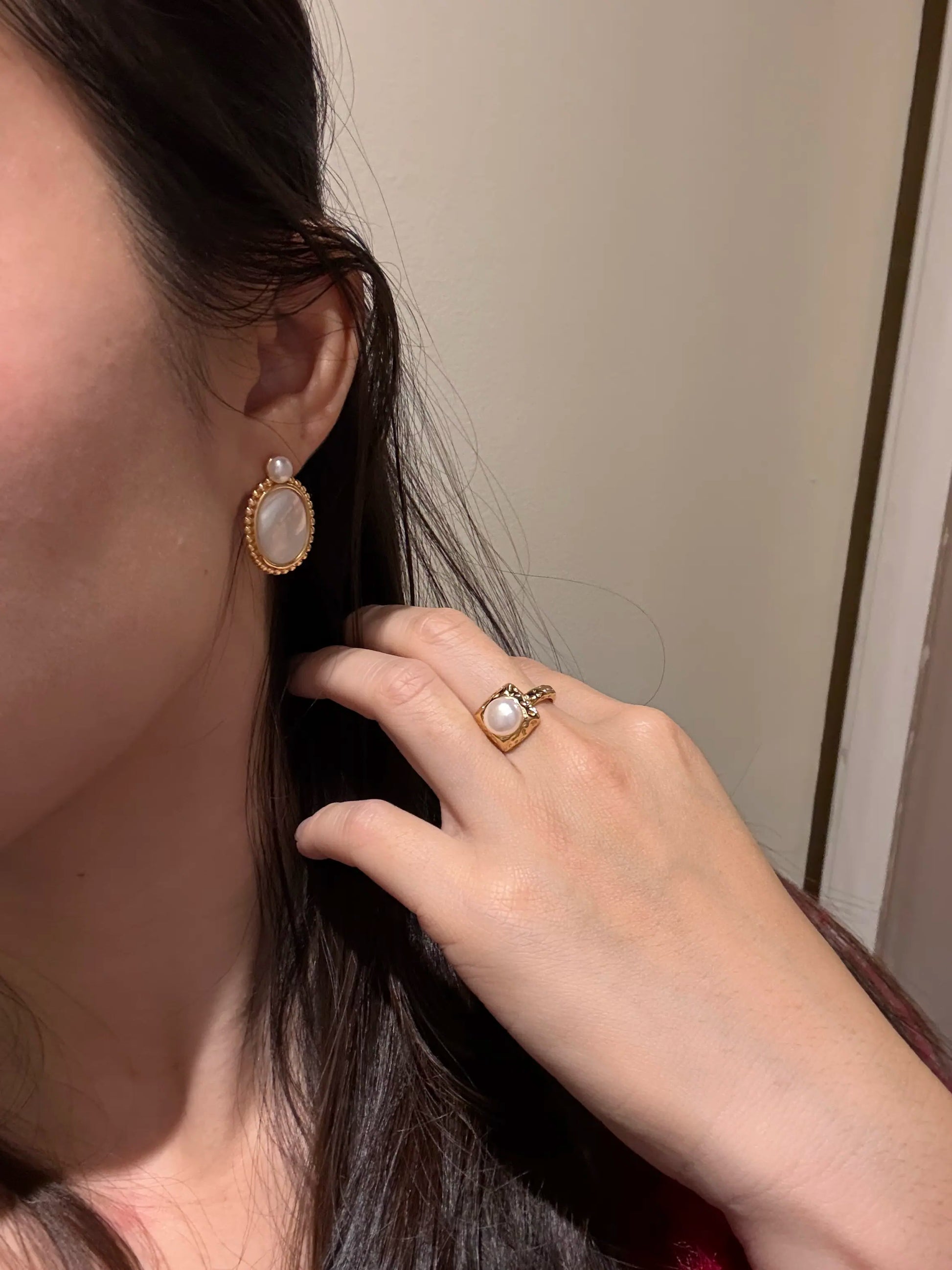 Close-up of a hand adjusting hair with earrings on a neutral background