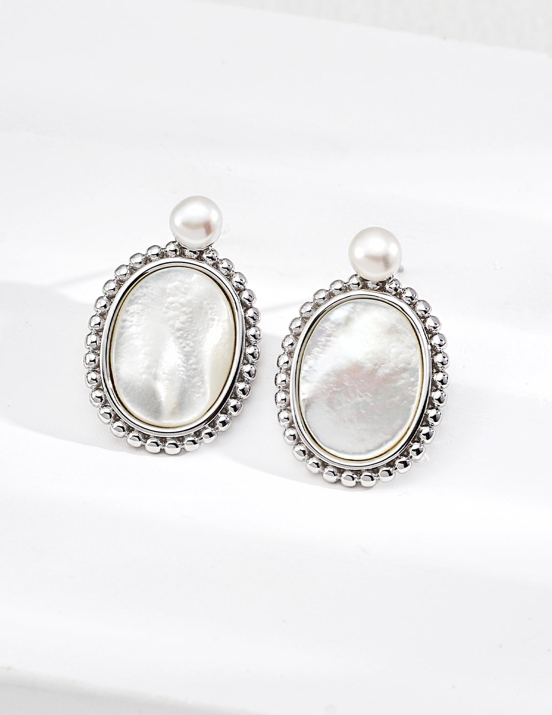 Pair of silver earrings with pearl-like stones on a white background