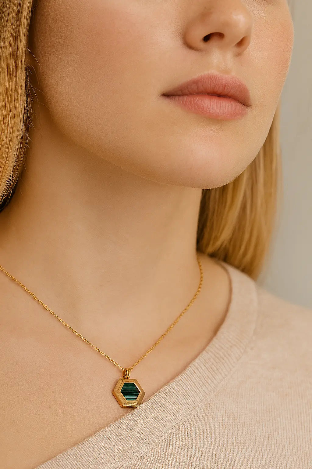 Close-up of a young woman wearing a gold hexagon malachite pendant necklace, styled on fair skin with a beige knit top — elegant gemstone jewellery handcrafted for modern women in the UK.