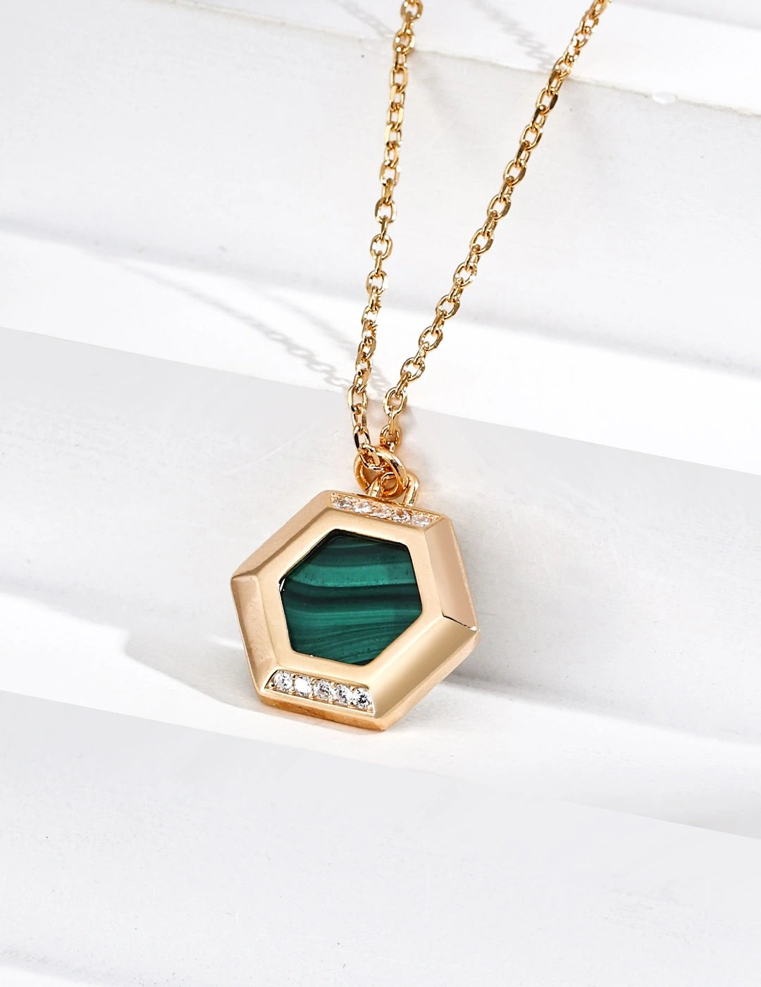 Gold necklace with a hexagonal pendant featuring a green stone on a white background