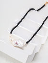 Elegant necklace featuring polished black onyx beads leading to a central large baroque pearl flanked by smaller pearls, displayed artistically on a white, tiered platform