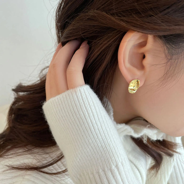 Woman with brown hair wearing elegant gold oval stud earrings, styled with a cozy white sweater - anais&aimee.com