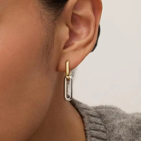 Close-up image of a woman wearing Ovate Double Mixed Metal Link Hoop Earrings by Anais & Aimee. The earrings feature a sleek, modern design with a combination of gold and silver metals.