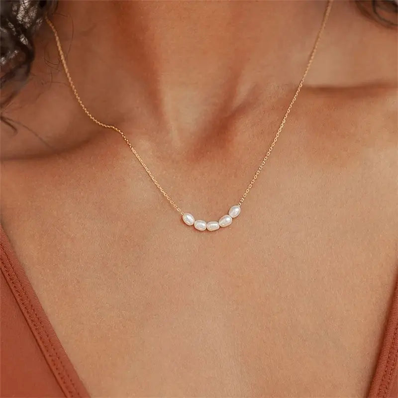 Close-up of a woman wearing a Rose Gold Freshwater Pearl Necklace, featuring a delicate rose gold chain adorned with small, lustrous freshwater pearls, gracefully highlighting her neckline.