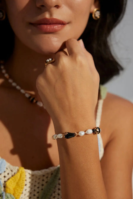 Close-up of the Serenity Black Obsidian Pearl Bracelet by Anaïs & Aimee on a model’s wrist. The gold accents, black obsidian, and pearls shine against a soft and stylish outfit