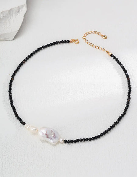 The Serenity Black Obsidian Pearl Necklace - 44cm, laid out in a circular design, showcasing its clasp and delicate craftsmanship by Anaïs & Aimee.