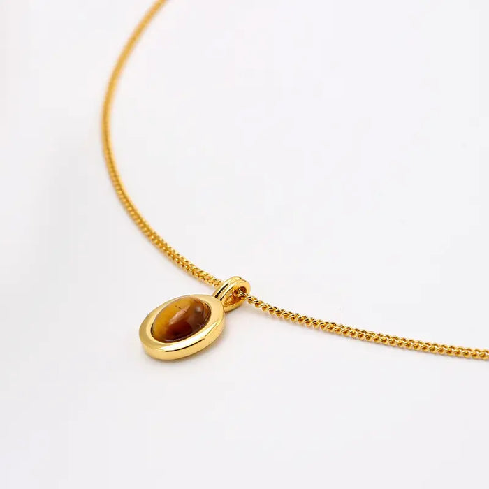 Close-up of a gold chain necklace with an oval tiger eye gemstone pendant, showcasing its captivating brown and golden tones against a white background.