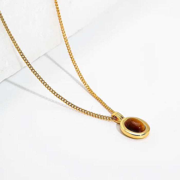 Close-up of a gold chain necklace featuring an elegant oval tiger eye gemstone pendant, highlighting its rich brown and golden hues.