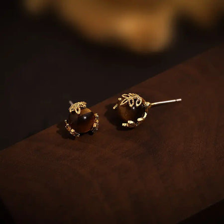 Stunning Anais & Aimee Tiger’s Eye Juniper Stud Earrings with polished tiger’s eye gemstones, encased in gold-plated juniper leaf designs, perfect for adding a touch of elegance to any outfit.