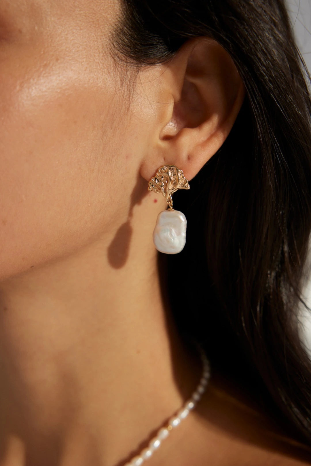 Close-up of a woman wearing gold earrings with a white pearl drop.