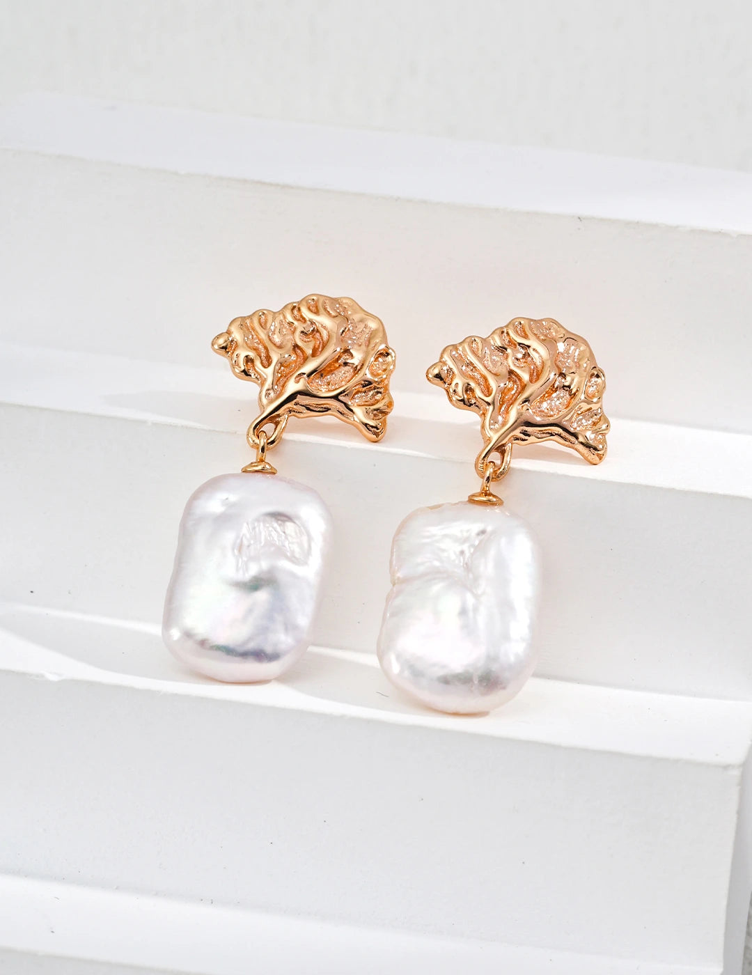 Gold earrings with pearl drops on a white background