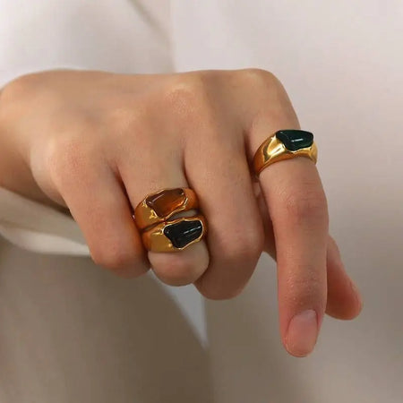 Woman wearing Tri-Color Gemstone Gold Signet Rings, featuring polished gold-tone bands with vibrant gemstone accents in black, green, and amber hues. These high trending accessories add a touch of bold elegance and sophistication, perfect for making a stylish statement.
