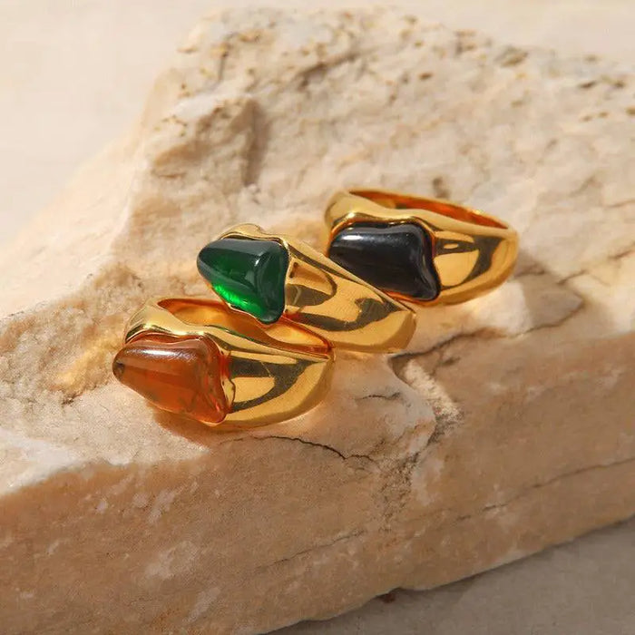 Tri-Color Gemstone Gold Signet Rings featuring polished gold-tone bands with vibrant gemstone accents in black, green, and amber hues, displayed on a natural stone surface. These high trending accessories add a touch of bold elegance and sophistication, perfect for making a stylish statement.