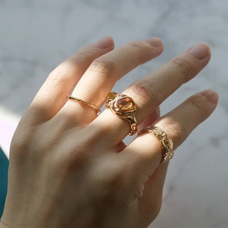 Trio Adjustable Gold Ring Set featuring three rings on a hand - one with an amber gemstone, a hammered design ring, and a delicate open-ended wavy pattern ring, showcasing their unique textures and adjustable fit.