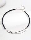 Elegant black agate necklace featuring a silver evil eye pendant with a black gem center, linked to a silver chain extension for adjustable length, all set against a textured white background.