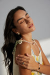 A woman posing with eyes closed, wearing the Vintage Grace Pearl and Enamel Ring, matching earrings, and a pearl necklace. The gold ring and earrings feature a black enamel square with a delicate floral pearl design, radiating vintage elegance and sophistication. The overall look is serene and stylish, enhanced by the soft lighting.