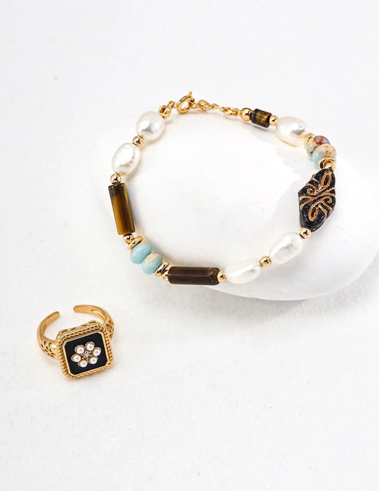 A styled set featuring the Vintage Grace Pearl and Enamel Ring and a coordinating bracelet. The gold ring showcases a black enamel square with a floral pearl design, while the bracelet is adorned with freshwater pearls, gemstones, and intricate gold accents. Both pieces radiate vintage charm and elegance, displayed against a white background.