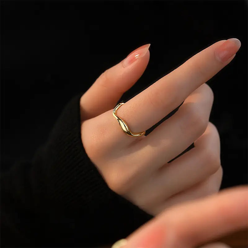 Elegant Wanstead Gold Cuff Ring - Adjustable with a wavy design, beautifully worn on a finger, accentuating its sleek and modern look against a dark background.