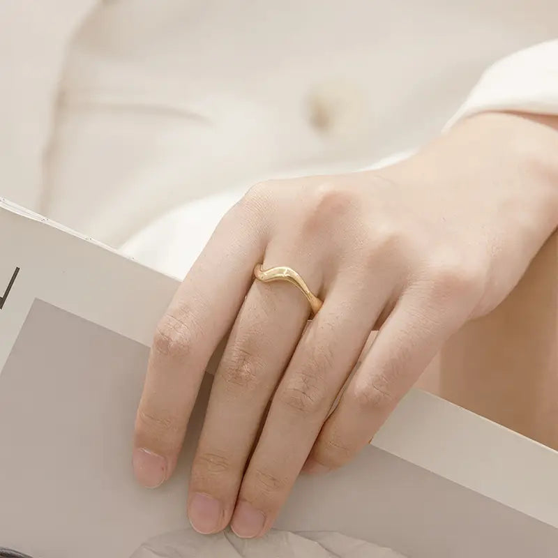 Stylish Wanstead Gold Cuff Ring - Adjustable with a unique wavy design, elegantly worn on a hand holding a magazine, highlighting its chic and modern appeal.