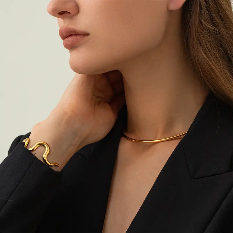 Close-up of woman wearing gold wave cuff bracelet and simple gold choker with black blazer
