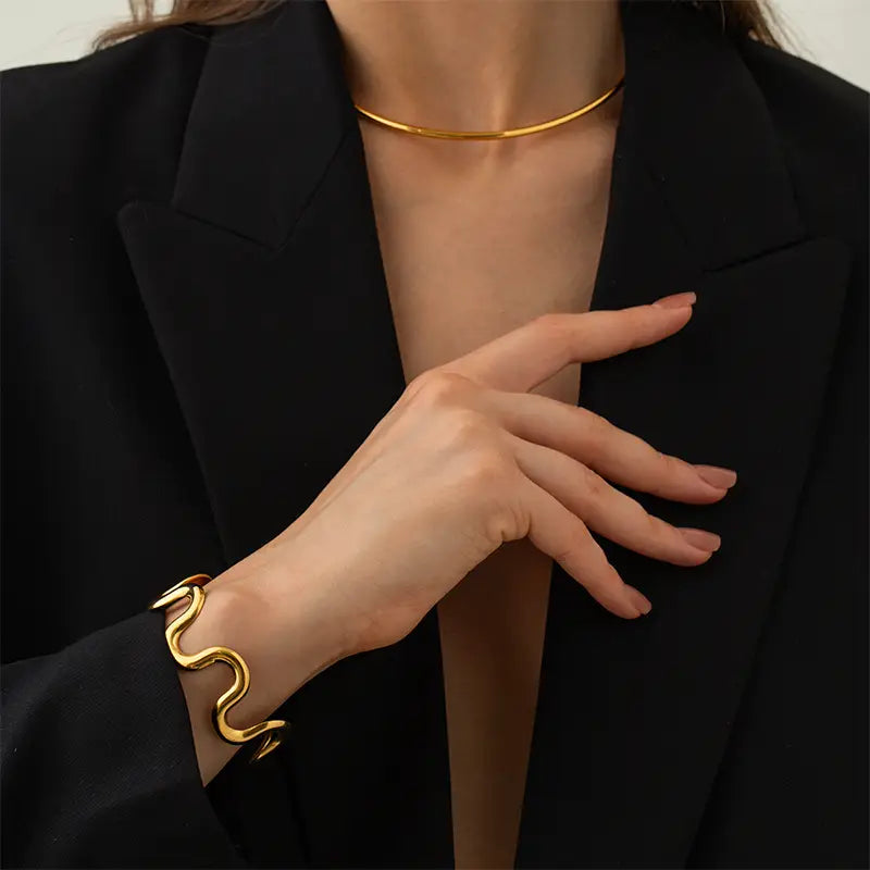Close-up of woman wearing gold wave cuff bracelet and choker necklace with black blazer.