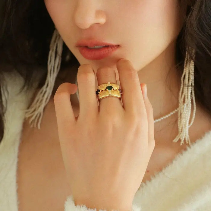 Woman wearing the Radiance Gemstone Ring, showcasing an intricate gold-tone design with detailed texturing and vibrant gemstones in green, purple, and red. These high trending hoop earrings add luxury and elegance, making a bold fashion statement. She is dressed in a white outfit with pearl accessories, enhancing the earrings' sophisticated appeal.